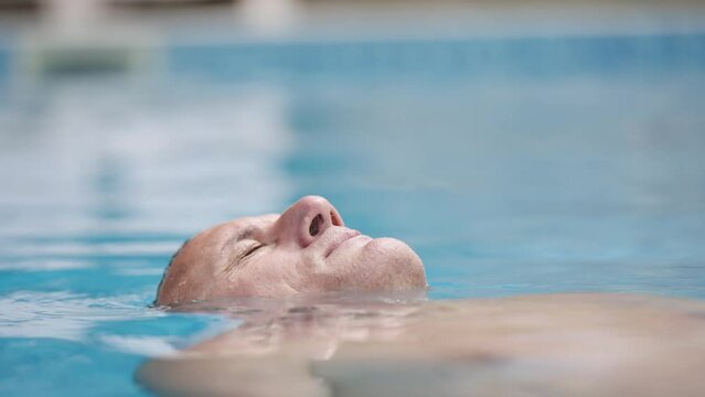 Happy man relaxing lying in a swimming pool on a sunny day, slow motion