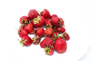 Heap of fresh ripe natural strawberries on a white saucer. Freshly picked garden strawberries. Detailed photo of strawberries on an abstract background. Close up view