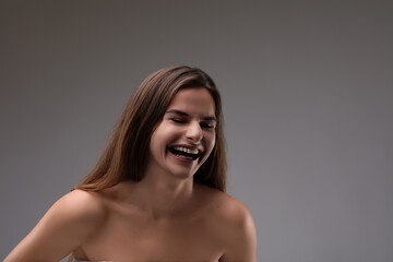 Obraz premium Beautiful young woman with long brown hair is laughing on a gray