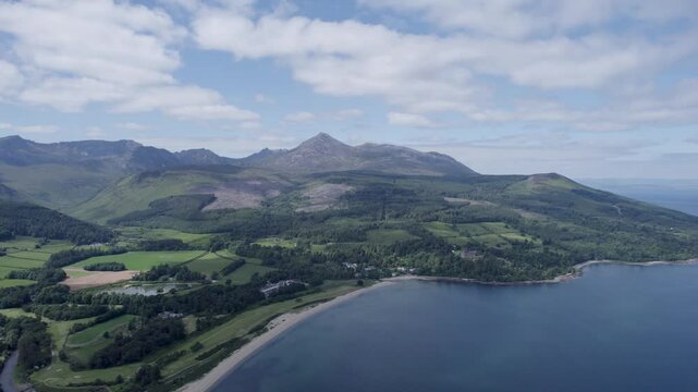 Aerial view of the coast on a sunny day with green hills, cliffs, and blue ocean water of the Isle of Arran, scotland