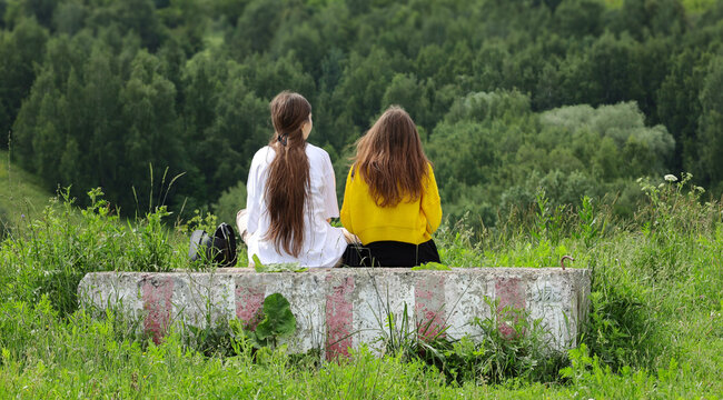 Two girls friends communicate in nature. Two young girls are sitting in the park with their backs turned.