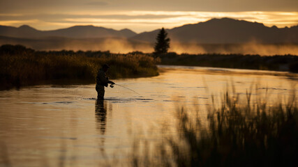 man fishing in a river in the wilderness during sunset or sunrise 