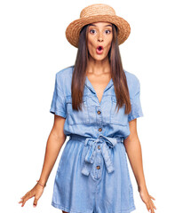 Fototapeta premium Young hispanic woman wearing summer hat scared and amazed with open mouth for surprise, disbelief face