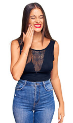 Young hispanic woman wearing casual clothes touching mouth with hand with painful expression because of toothache or dental illness on teeth. dentist