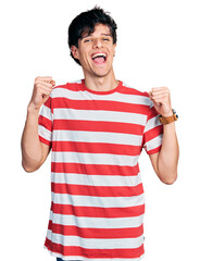 Fototapeta premium Handsome hipster young man wearing casual striped t shirt celebrating surprised and amazed for success with arms raised and open eyes. winner concept.
