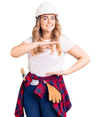 Young caucasian woman wearing security helmet gesturing with hands showing big and large size sign, measure symbol. smiling looking at the camera. measuring concept.