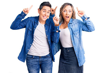 Couple of women wearing casual clothes smiling amazed and surprised and pointing up with fingers and raised arms.