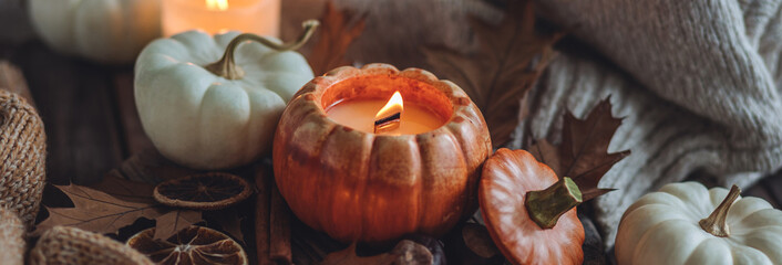 Atmospheric candle - shape of pumpkins, autumn decor on grey fall rainy day. Autumn cozy home atmosphere and inspiration, hygge concept. Aromatherapy, warming, relaxation. Wooden background banner