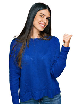 Young hispanic woman wearing casual clothes smiling with happy face looking and pointing to the side with thumb up.