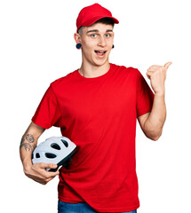 Young caucasian boy with ears dilation wearing delivery uniform and cap holding bike helmet...