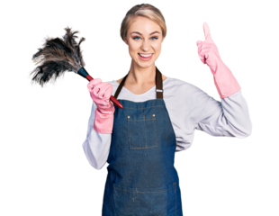 Beautiful young blonde woman wearing apron holding cleaning duster smiling amazed and surprised and pointing up with fingers and raised arms.