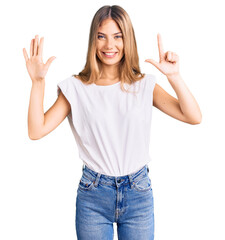 Beautiful caucasian woman with blonde hair wearing casual white tshirt showing and pointing up with fingers number seven while smiling confident and happy.