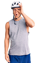 Fototapeta premium Young handsome man wearing bike helmet doing ok gesture shocked with surprised face, eye looking through fingers. unbelieving expression.