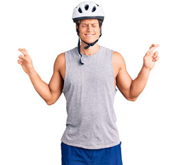 Young handsome man wearing bike helmet gesturing finger crossed smiling with hope and eyes closed. luck and superstitious concept.