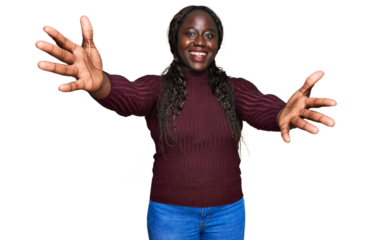 Young african woman wearing casual winter sweater looking at the camera smiling with open arms for hug. cheerful expression embracing happiness.