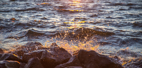 The tide hits the rocks and stirs up crystal-like water drops at sea sunset, vacation concept background