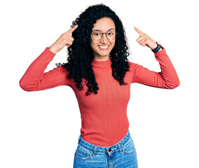 Young hispanic woman with curly hair wearing glasses smiling pointing to head with both hands finger, great idea or thought, good memory