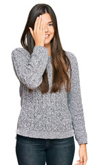 Young brunette woman wearing casual winter sweater covering one eye with hand, confident smile on face and surprise emotion.