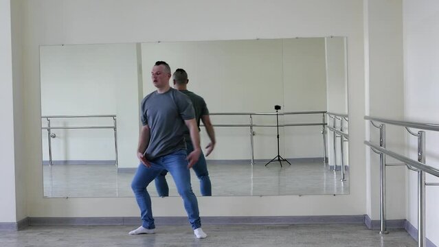 Male dance choreography ballet in the hall, a man dances in jeans in the fitness room. A handsome young guy makes simple dance movements