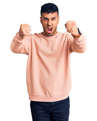 Young hispanic man wearing casual clothes angry and mad raising fists frustrated and furious while shouting with anger. rage and aggressive concept.