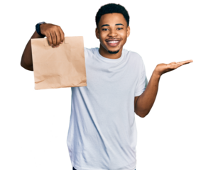 Young african american man holding take away paper bag celebrating achievement with happy smile and winner expression with raised hand