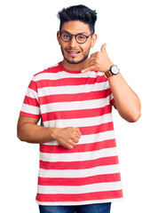 Handsome latin american young man wearing casual clothes and glasses smiling doing phone gesture with hand and fingers like talking on the telephone. communicating concepts.