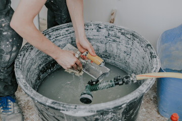 A young builder washes spatulas in a basin.