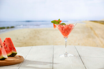 Watermelon coctail in glass on white table top and blur background of sandy beach and sea and blue sky.  Empty space for products and food.
