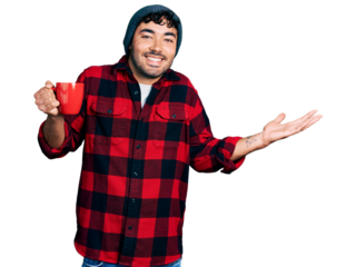 Hispanic young man with beard drinking a cup of coffee celebrating achievement with happy smile and winner expression with raised hand