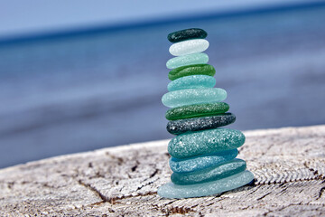Stable balanced cairn of polished sea glass stones on a wooden log on the seashore