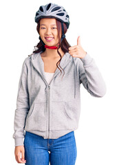 Young beautiful chinese girl wearing bike helmet smiling happy and positive, thumb up doing excellent and approval sign