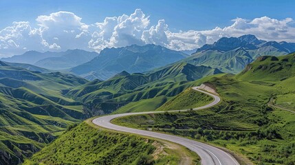 Fototapeta premium Paved road curving through green mountains, set against a backdrop of a clear sky with cumulus clouds