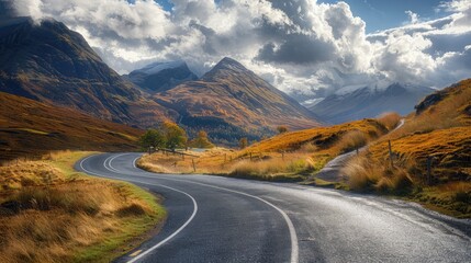 Fototapeta premium Scenic road winding through mountains under a bright sky with fluffy clouds in the background