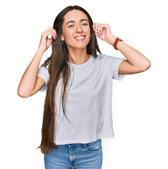 Young hispanic girl wearing casual white t shirt smiling pulling ears with fingers, funny gesture....