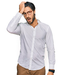 Young hispanic man wearing business shirt and glasses surprised with hand on head for mistake, remember error. forgot, bad memory concept.