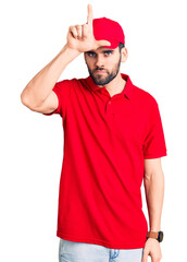 Young handsome man with beard wearing delivery uniform making fun of people with fingers on forehead doing loser gesture mocking and insulting.