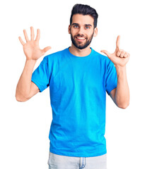 Naklejka premium Young handsome man with beard wearing casual t-shirt showing and pointing up with fingers number seven while smiling confident and happy.