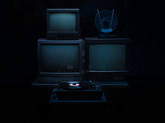 3 vintage television receivers with antenna and record player on a dark background