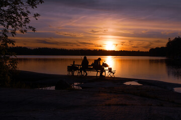 A group of people are sitting on a bench by a lake, watching the sun set