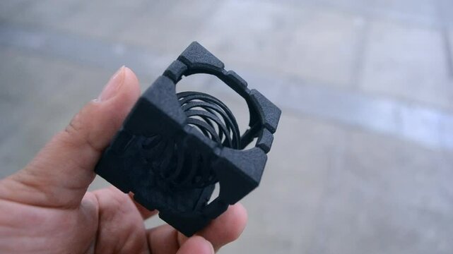 A person holding in his hand an object printed on a 3D printer. Geometric model printed on a 3D printer from molten plastic close-up. Black shape created by 3D printer. FDM technology.