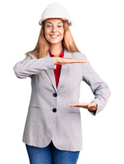 Beautiful young woman wearing architect hardhat gesturing with hands showing big and large size sign, measure symbol. smiling looking at the camera. measuring concept.