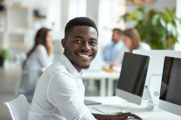 Fototapeta premium Happy young black African American man employee in front of computer in modern office with colleagues. Beautiful manager smiling, working on financial and marketing projects