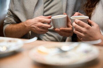 Girlfriend and boyfriend is sitting in restaurant holding coffee in their hands