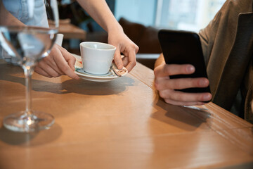 Young man having coffee and using mobile phone at restaurant