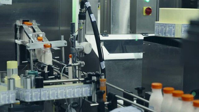 Automated machinery is operating at a production plant. Automated machinery is sticking the labels to the bottles with the product. Automated machinery placing the label on the product. Manufacturing.