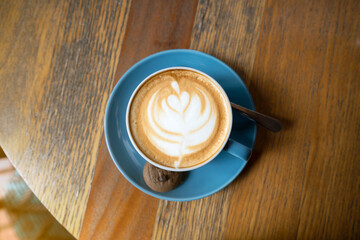 A blue coffee cup with a white leaf design on it sits on a wooden table