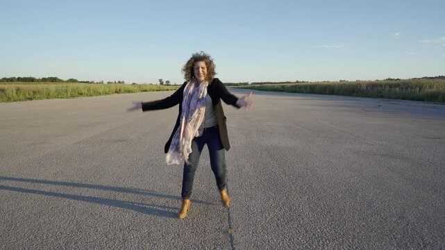 Mujer caminando y dando saltos y vueltas de alegr&iacute;a con los brazos en alto, en una pista de aterrizaje.