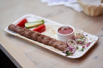 Beef kebab on a white rectangular plate with vegetables. Lula is a kebab with cucumbers, red pepper and round onion slices. With space to copy. High quality photo