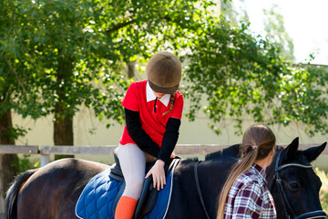 Young rider adjusts helmet on horseback under trees.