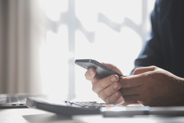 Side view shot of a man's hands using smart phone in interior, rear view of business man hands busy using cell phone at office desk, young male student typing on phone sitting at wooden table, flare